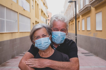 couple of two seniors wearing medical mask to prevent coronavirus (covid-19) or another type of virus - close up of faces in middle of street - protect people satying safe together - italian people
