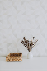 Stylish minimalistic wall space with dried flowers in a white vase, standing on a drawer at home or studio. Copy space.