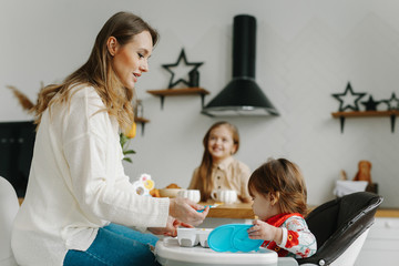Mom feeding her adorable baby girl healthy food with spoon at home