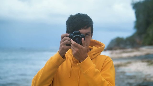 Male photographer in a yellow hoodie takes a photo on a beautiful wild tropical beach in the evening