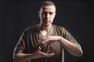 Fototapeta na wymiar Young professional massage therapist flexes his hands before massage while standing against a dark background