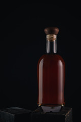 Glass bottle filled with brandy or whisky on black background. Bottle of alcoholic drink on wooden table.