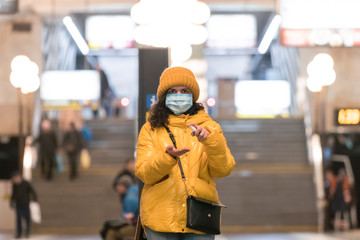 The young europeans woman in protective disposable medical face mask using antiseptic in the subway. New coronavirus (COVID-19).