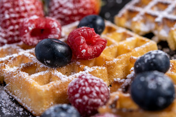 Homemade sweet waffles in the shape of a heart, with berry fruits and powdered sugar. With fresh blueberries and raspberries.