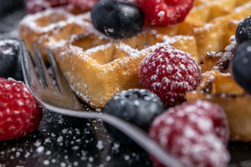Homemade sweet waffles in the shape of a heart, with berry fruits and powdered sugar. With fresh blueberries and raspberries.