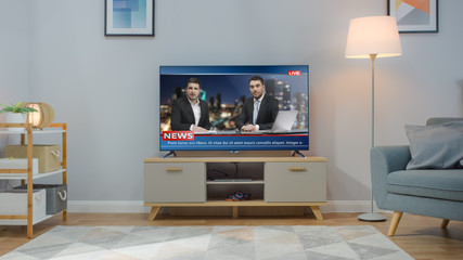 Shot of a TV with Live News Channel. Cozy Living Room at Day Time with a Chair and Lamps Turned On...