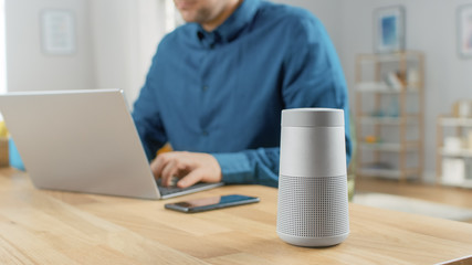 Close Up Shot of a Modern Silver Bluetooth Speaker Standing on a Table at Home. Man in the...