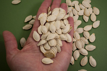 pile of  pumpkin seeds in hand on green background, eating