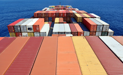 View on the containers loaded on deck of the large cargo ship. She is sailing through calm, blue...