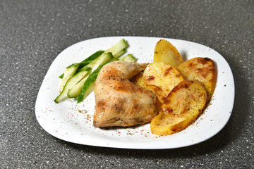 Fried chicken with potatoes on a white plate on a gray granite table