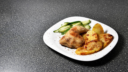 Fried chicken with potatoes on a white plate on a gray granite table