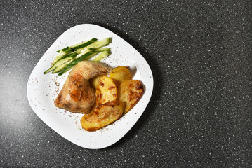 Fried chicken with potatoes on a white plate on a gray granite table