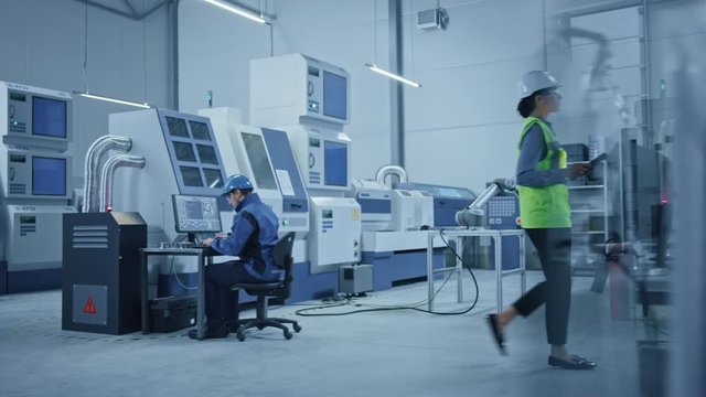 In Factory: Professionals Working on CNC Machinery, Walk Through Workshop, Use Digital Tablet, Manipulate Robot Arm Production Line. In-Office: Engineer Controls System with Computer. Moving Camera