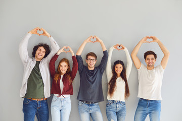 Group of friends making a heart with hands smiling while standing on gray background.