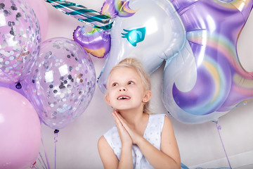 cute blonde girl with a balloon unicorn makes a birthday wish © edelweiss7227