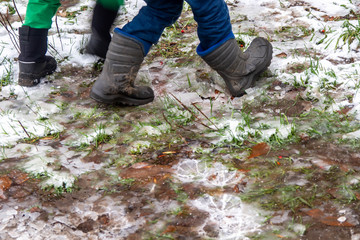 Children run on the first snow. Feet in boots close-up. The child breaks the ice with his boot.