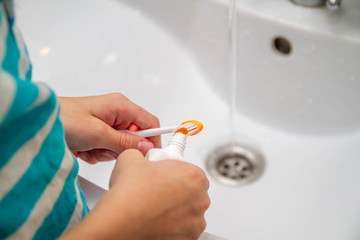 Squeeze toothpaste onto a toothbrush from a tube in the bathroom at home. The boy wants to brush his teeth.
