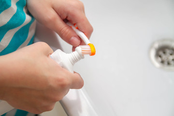 Squeeze toothpaste onto a toothbrush from a tube in the bathroom at home. The child wants to brush his teeth in the morning after eating.