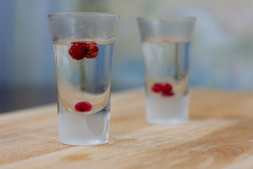 ice-cold vodka glasses with raspberries and currants on a wooden stand