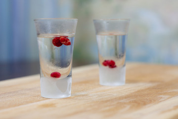 ice-cold vodka glasses with raspberries and currants on a wooden stand