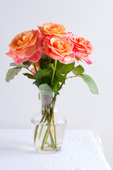 Obraz premium Glass vase with beautiful bouquet of fresh natural roses flowers on a table covered white cloth against light grey wall.