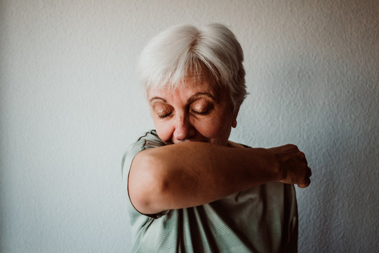 .White-haired, middle-aged woman with coronavirus symptoms coughing correctly on her elbow. Global health crisis. Pandemia