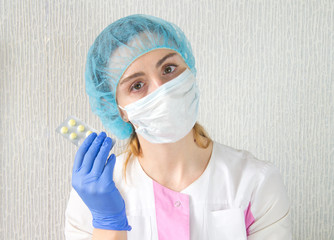 A nurse in a white mask and a cap in blue gloves holds a blister with pills in her hands. Russia