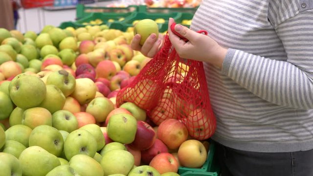 close-up hands of adult woman picking apples in supermarket and puts fruits on knitted mesh made of eco-friendly materials. selective focus