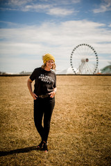 Portrait of happy woman wearing fashionable clothing with winter beanie hat, ferris wheel in the background and graphic t-shirt that says do what makes you happy. 