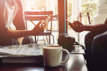 Coffee cup on wooden table in coffee shop and two handsome man is using a mobile phone - vintage style effect picture