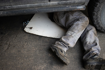 Mechanic in  uniform lying down and working under car at the garage.