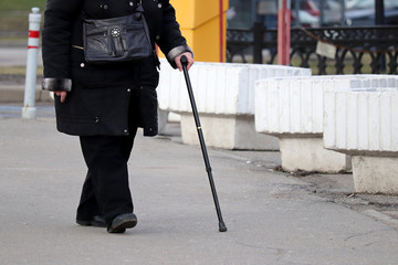 Elderly woman walking with a cane on a street, female legs on pavement. Concept for disability, limping person, diseases of the spine, old people