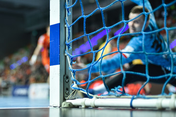 Detail of handball goal post with net and goalkeeper in the background. - obrazy, fototapety, plakaty