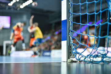 Detail of handball goal post with net and handball match in the background.