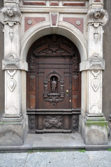 Fototapeta na wymiar An old carved wooden door, with elements of forging, framed by sculptures. The facade is in the Baroque style. Poland, Gdansk 2019.