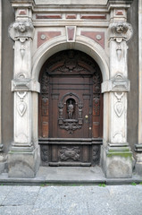 An old carved wooden door, with elements of forging, framed by sculptures. The facade is in the Baroque style. Poland, Gdansk 2019.