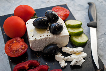 Greek salad recipe ingredients on a black chalkboard. Feta and other ingredients for Greek sala. Olives, cherry tomatoes.Photo for the menu.