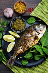 Roasted dorado fish with spices on a black plate. Nearby are lime, basil leaves and garlic. Healthy Diet Food