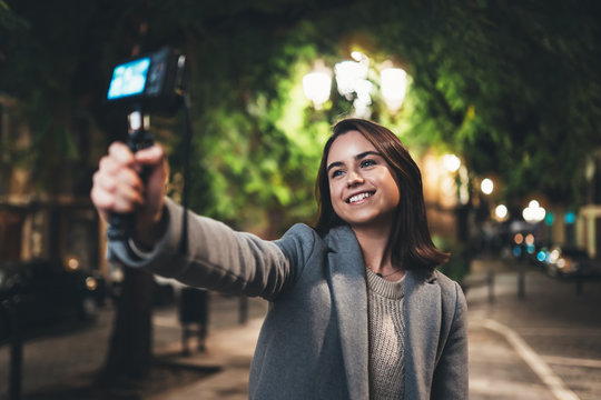 Female vlogger record with digital camera. Smiling woman taking selfie video on light night city. Traveler making video for her blog. Vlogger uses photo camera for shoot social media