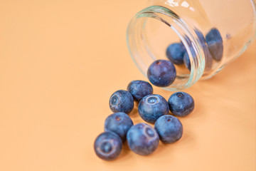 Blueberries fall out of a glass jar on an orange background.