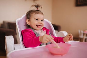 Little cute baby girl are eating in hight chair. Portrait of little smiled child at home