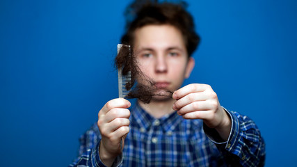 young man pulling clusters of hair from a comb as a result of hair loss