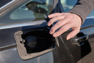 A man in a coat opens the gas tank to refuel the car.