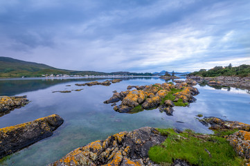 Sunset seascape with rocks in water and Skye island at the background. Hebrides archipelago, Scotland.