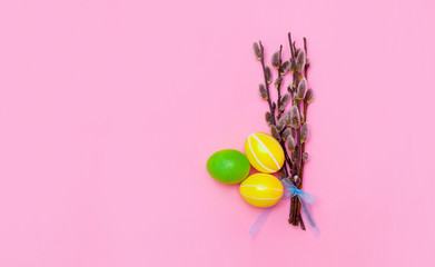 Three yellow and green eggs lie next to willow branches on a pink background. View from above. place for text. Banner. Easter card. Easter background. Easter.