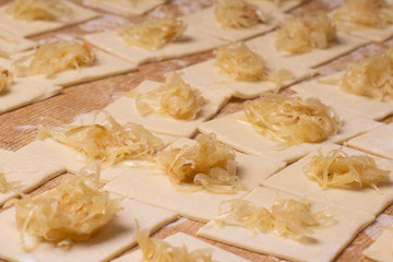 A rectangular piece of dough with cabbage - for making ravioli dumplings. Plywood cutting board, wooden flour sieve and wooden rolling pin - tools for making dough.