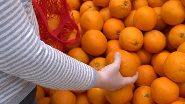 close-up hands of adult woman picking oranges in supermarket and puts fruits on knitted mesh made of eco-friendly materials. selective focus