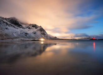 Mountains and reflections on beach at night. Winter landscape. The sky with stars and clouds in...