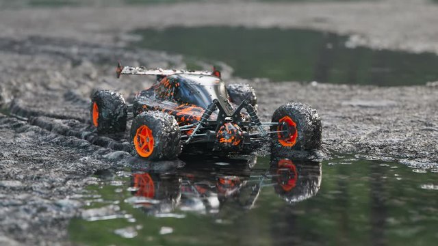 Dirty, orange RC-Car got stuck in the mud on a wet forest mire path. 4KHD