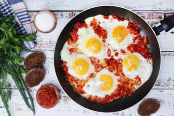 Shakshouka with five cooked eggs on top of tomato sauce in cast iron skillet	
